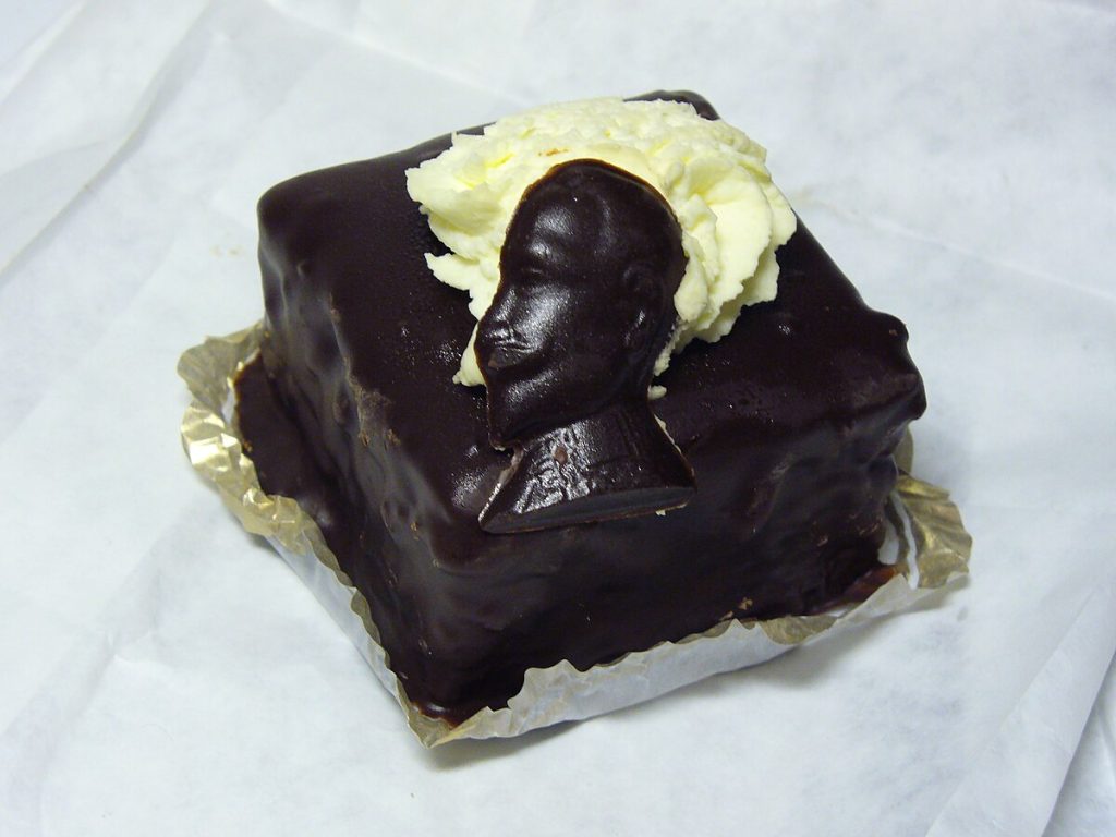Chocolate-covered Gustavus Adolphus pastry topped with whipped cream and a chocolate king profile