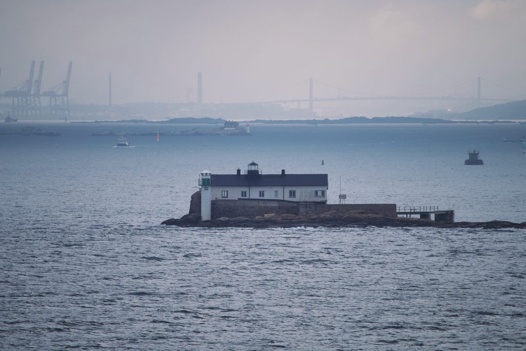 A small lighthouse and house building on a rocky island just off the coast of Gothenburg, Sweden, with the city skyline faintly in the background.
