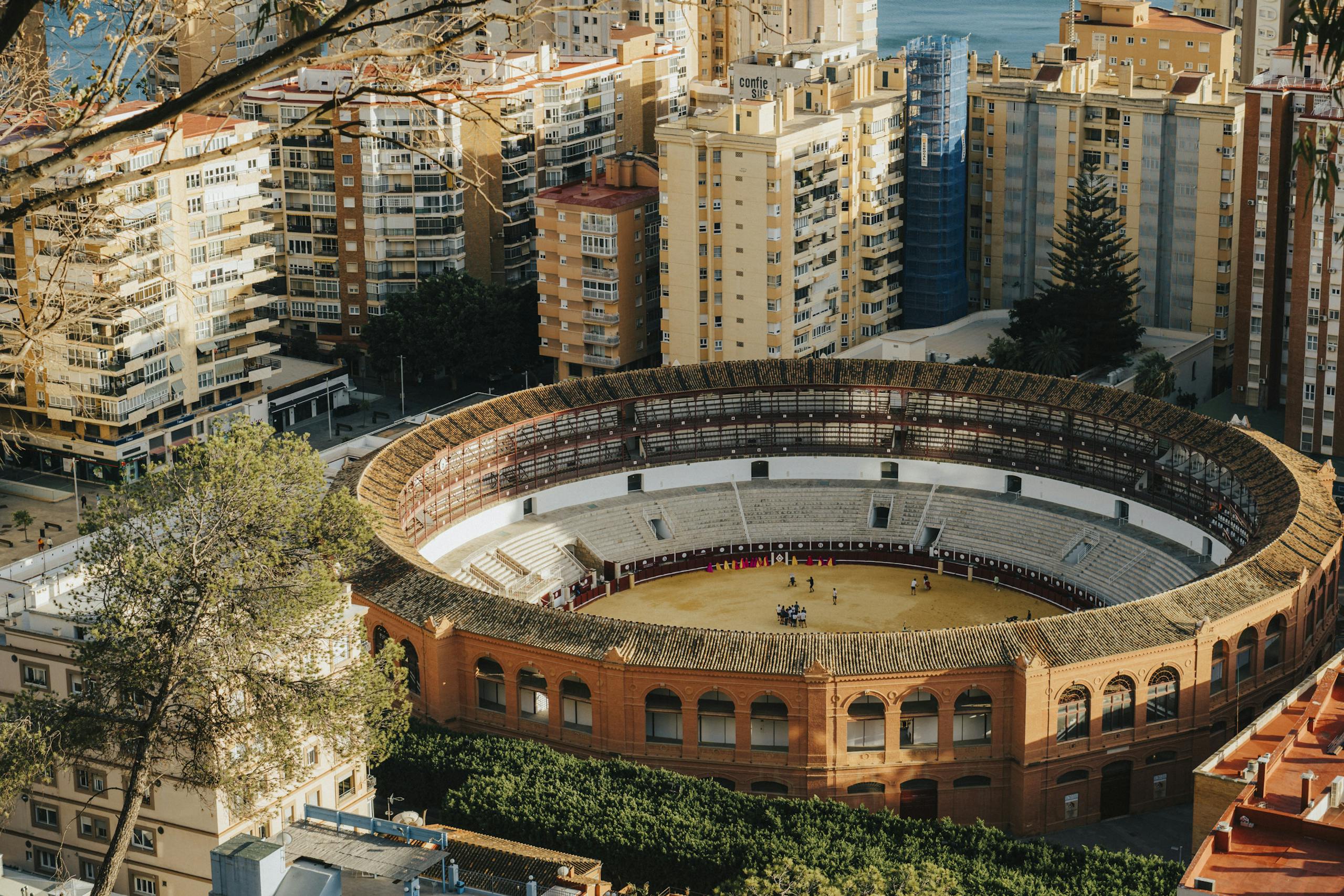Stunning aerial view of the Málaga bullring surrounded by cityscape and Mediterranean Sea.