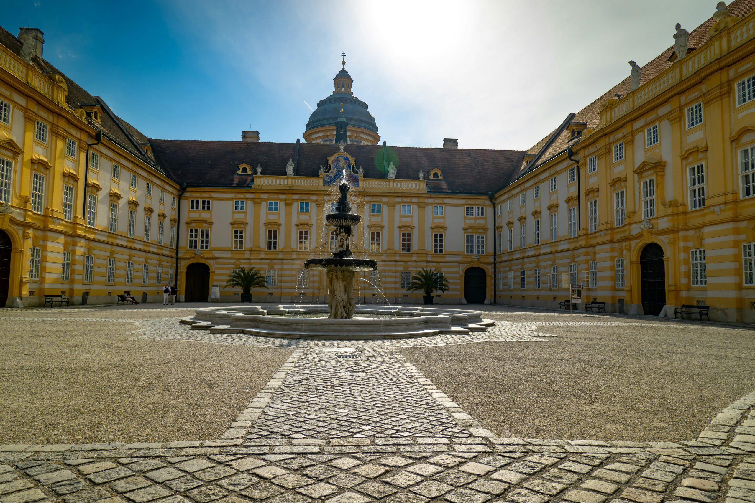 Melk Abbey courtyard with its central Baroque fountain and yellow facade under a bright afternoon sky