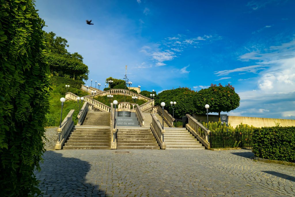 Grand staircase leading up to Melk Abbey, surrounded by manicured greenery and bright summer skies