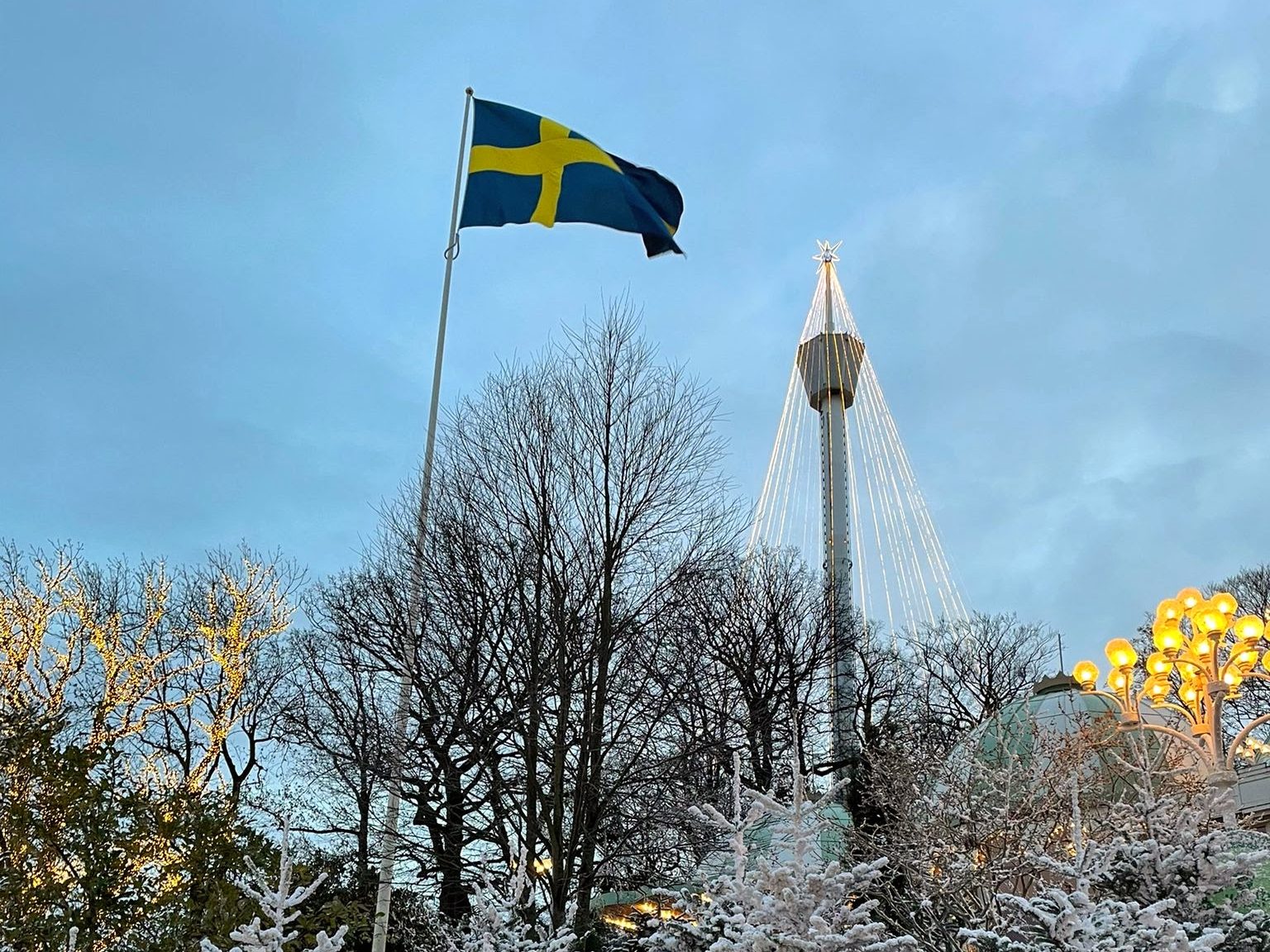 Swedish flag flying next to the illuminated Liseberg observation tower in Gothenburg during winter.
