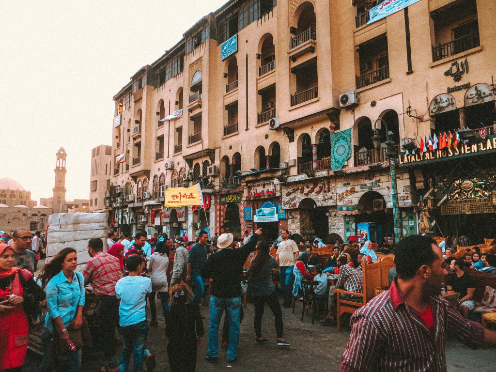 Crowded Cairo street scene with locals and tourists dining outdoors near traditional Egyptian buildings at sunset.