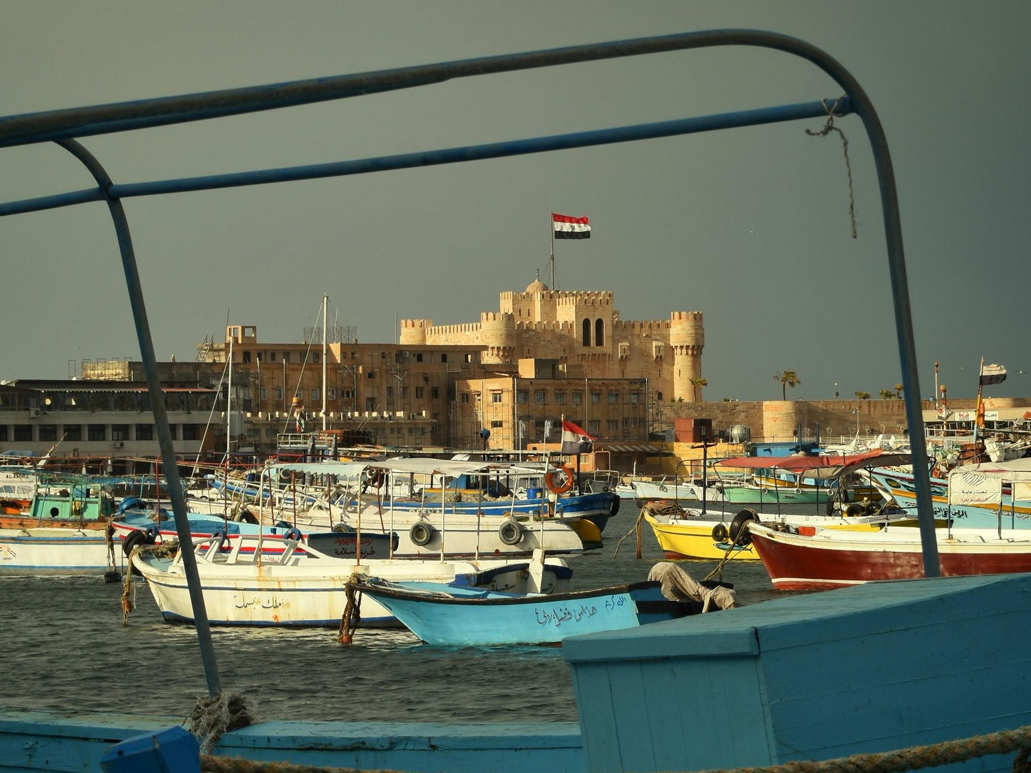 Colorful boats docked at Alexandria harbor with a view of the historic Qaitbay Citadel in Egypt.