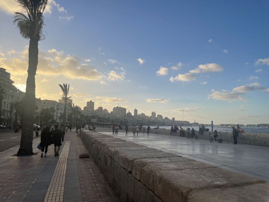 Evening stroll along the Alexandria Corniche with locals and palm trees at sunset.