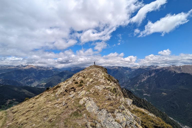 Garrett Landers standing on a rocky mountain ridge in Andorra with panoramic views of the Pyrenees under a partly cloudy sky.