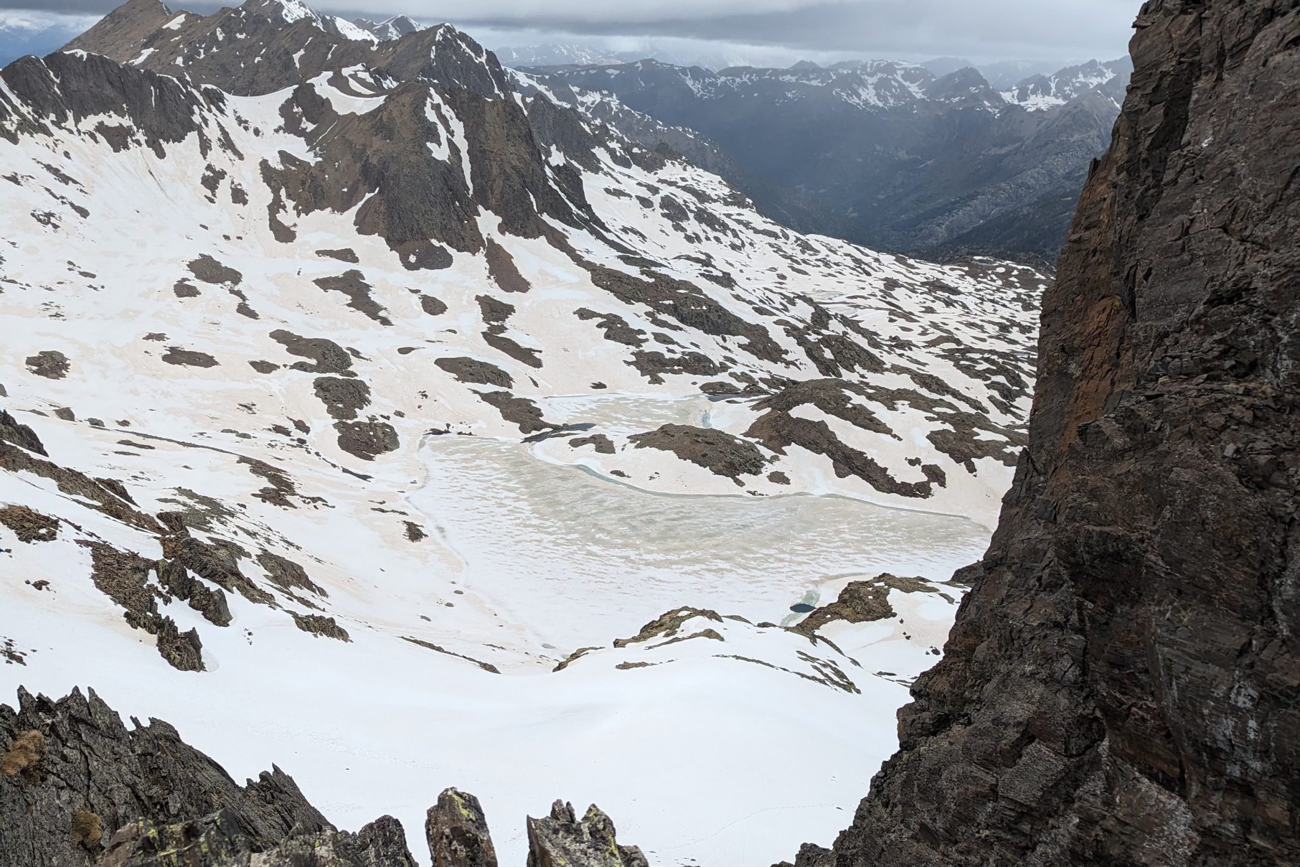 Snow-covered mountain valley with a partially frozen alpine lake seen from the Coma Pedrosa trail in Andorra.