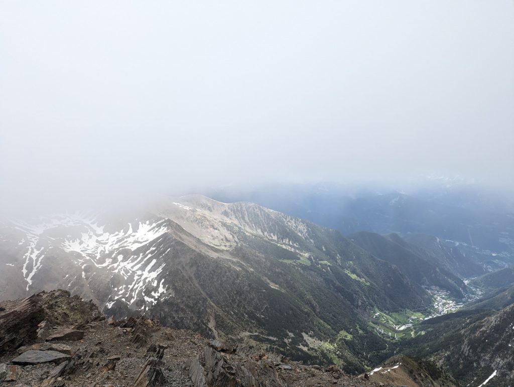 foggy view from the upper slopes of coma pedrosa in andorra with snow patches and steep pyrenees valleys below