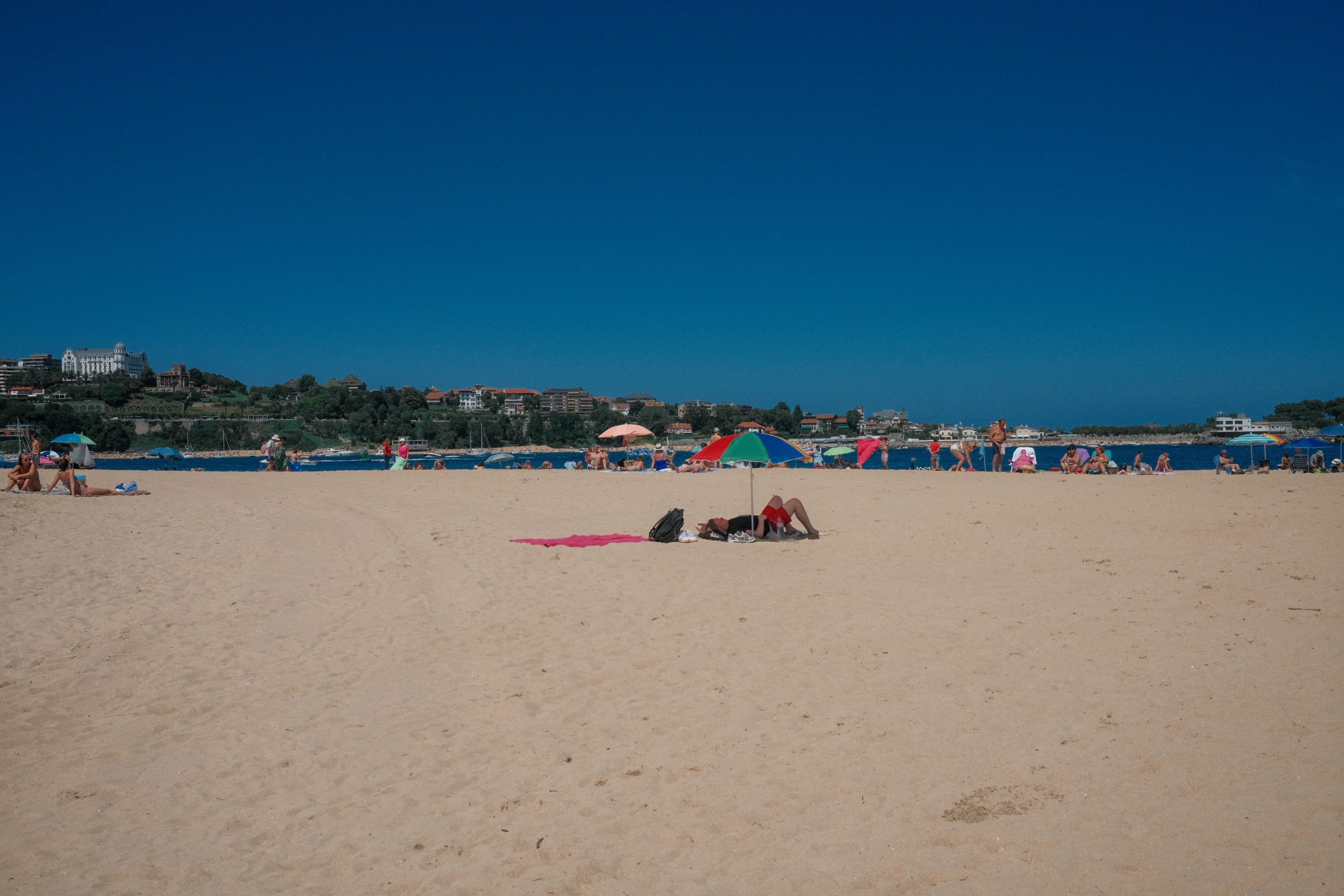 El Sardinero Beach in Santander, Spain, with umbrellas, sunbathers, and the Magdalena Palace in the background.