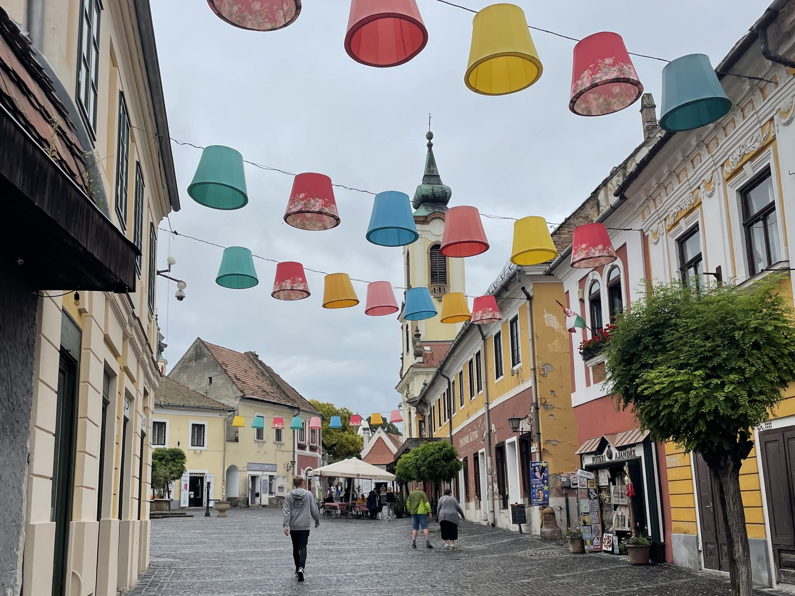 Colorful street in Szentendre, Hungary with hanging lamp shades, baroque buildings, and church tower