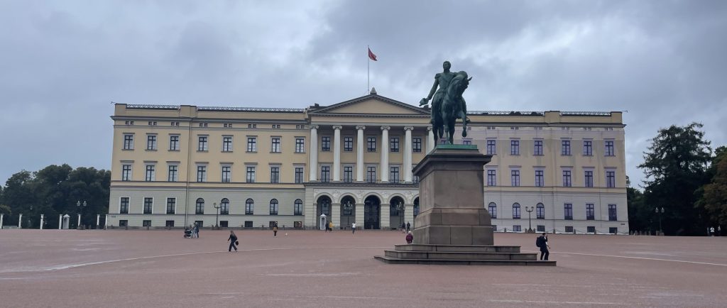 The Royal Palace in Oslo with the statue of King Karl Johan in front, seen on a cloudy September day with a few people walking across the open square.