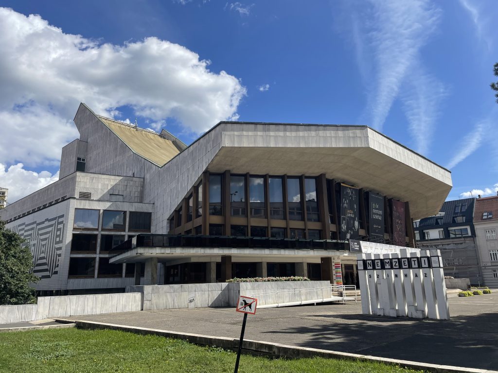 Győr National Theatre in Hungary, a modern concrete and glass building with bold geometric design under a bright blue sky.