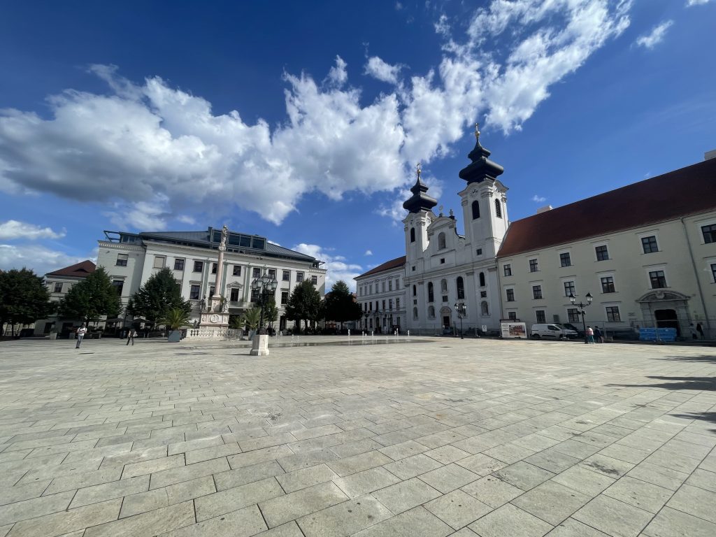 Cathedral Basilica of the Assumption of Our Lady in Széchenyi Square, Győr, Hungary, with baroque towers and blue skies above the plaza.