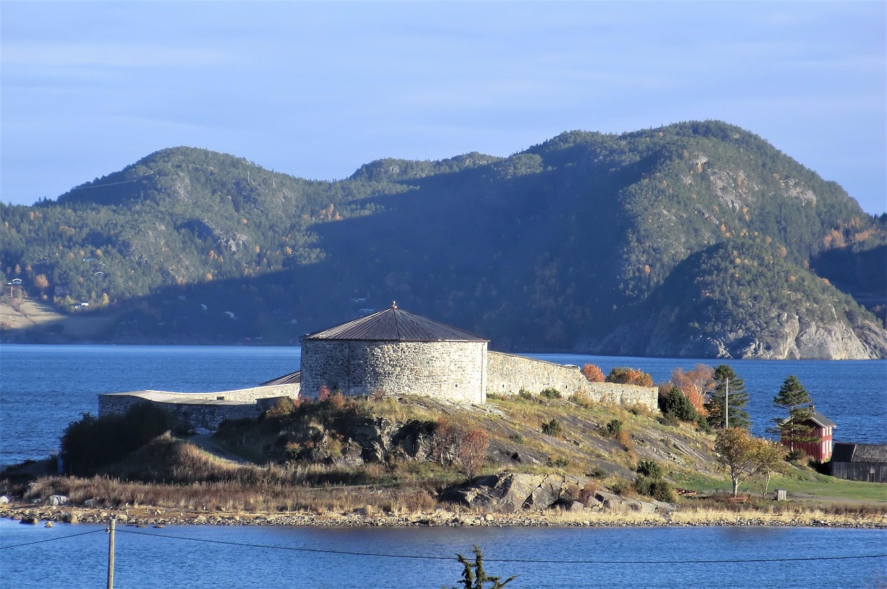 Munkholmen Island in Trondheim Fjord, Norway, featuring the historic stone fortress surrounded by calm blue water and forested hills.