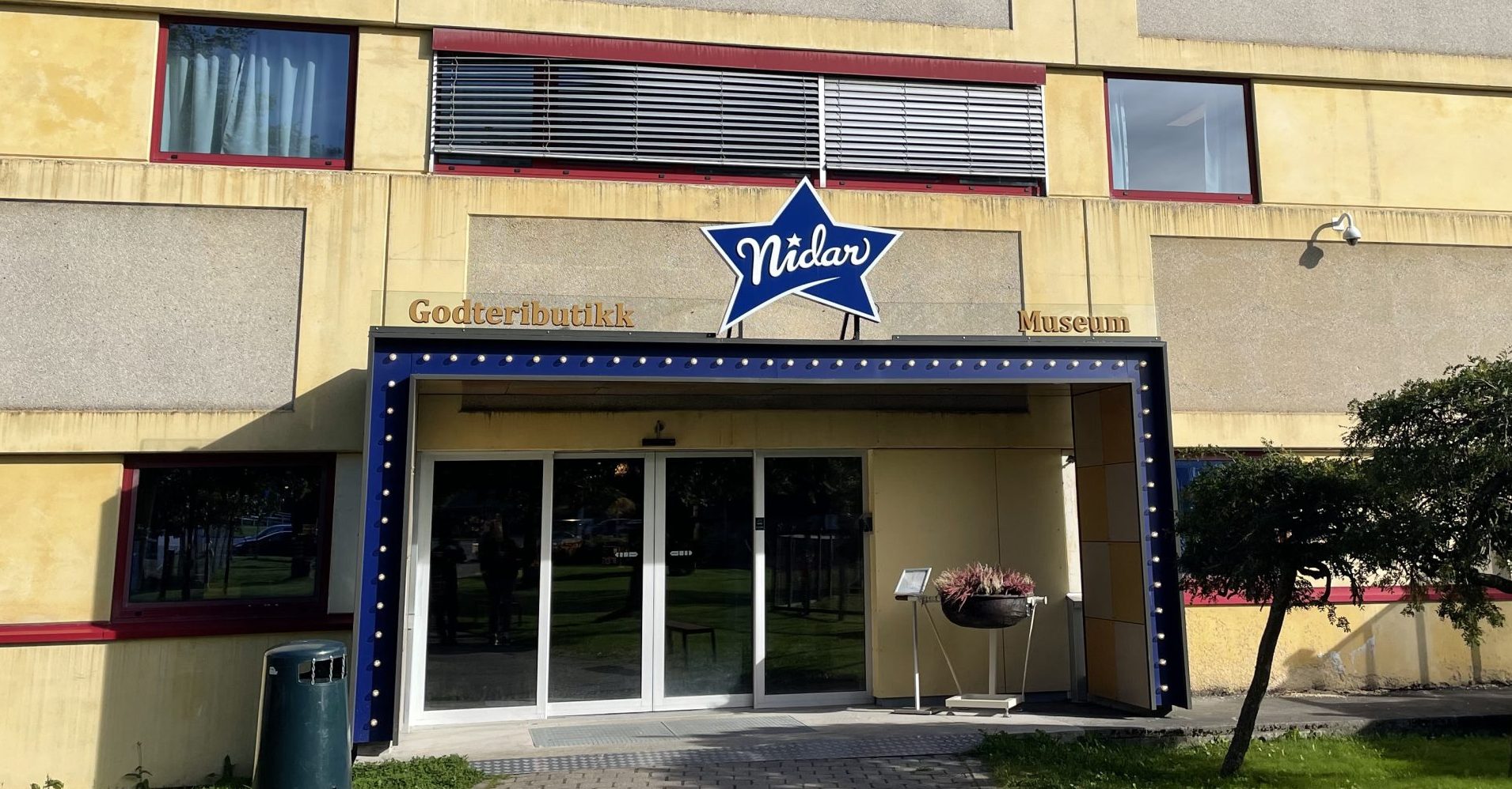 Exterior of Nidar Chocolate Factory and Godteributikk in Trondheim, Norway, under a bright blue sky.