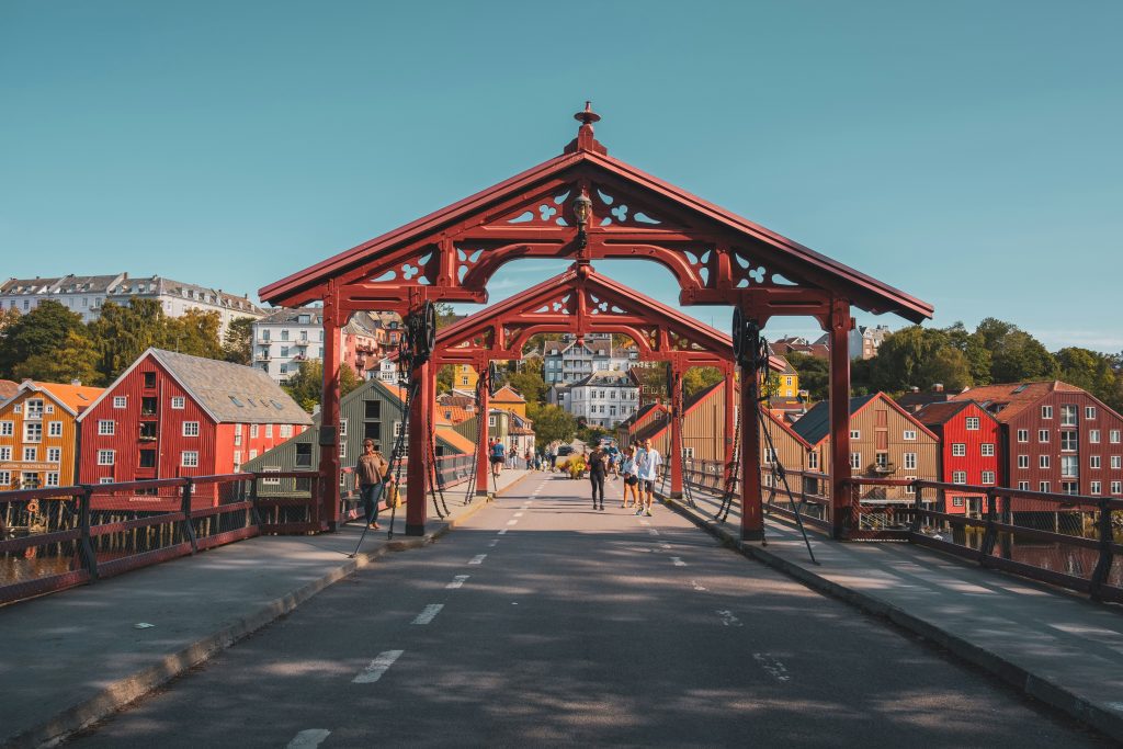 The red wooden Old Town Bridge (Gamle Bybro) in Trondheim, Norway, with colorful wooden houses along the Nidelva River.