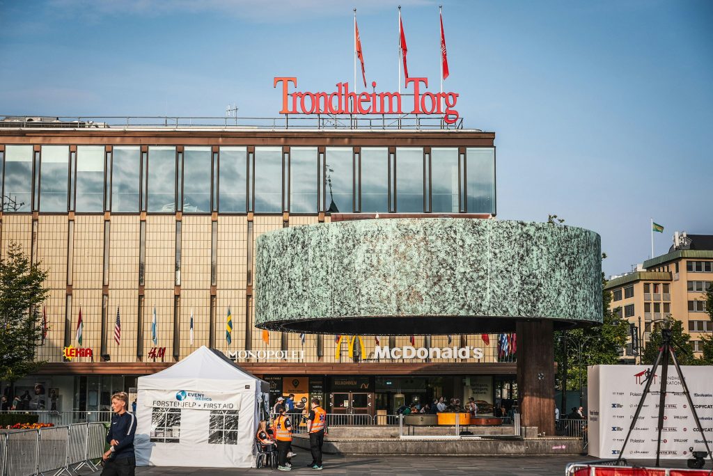 Trondheim Torg shopping square in central Trondheim, Norway, with flags, McDonald’s, and pedestrians on a sunny day.