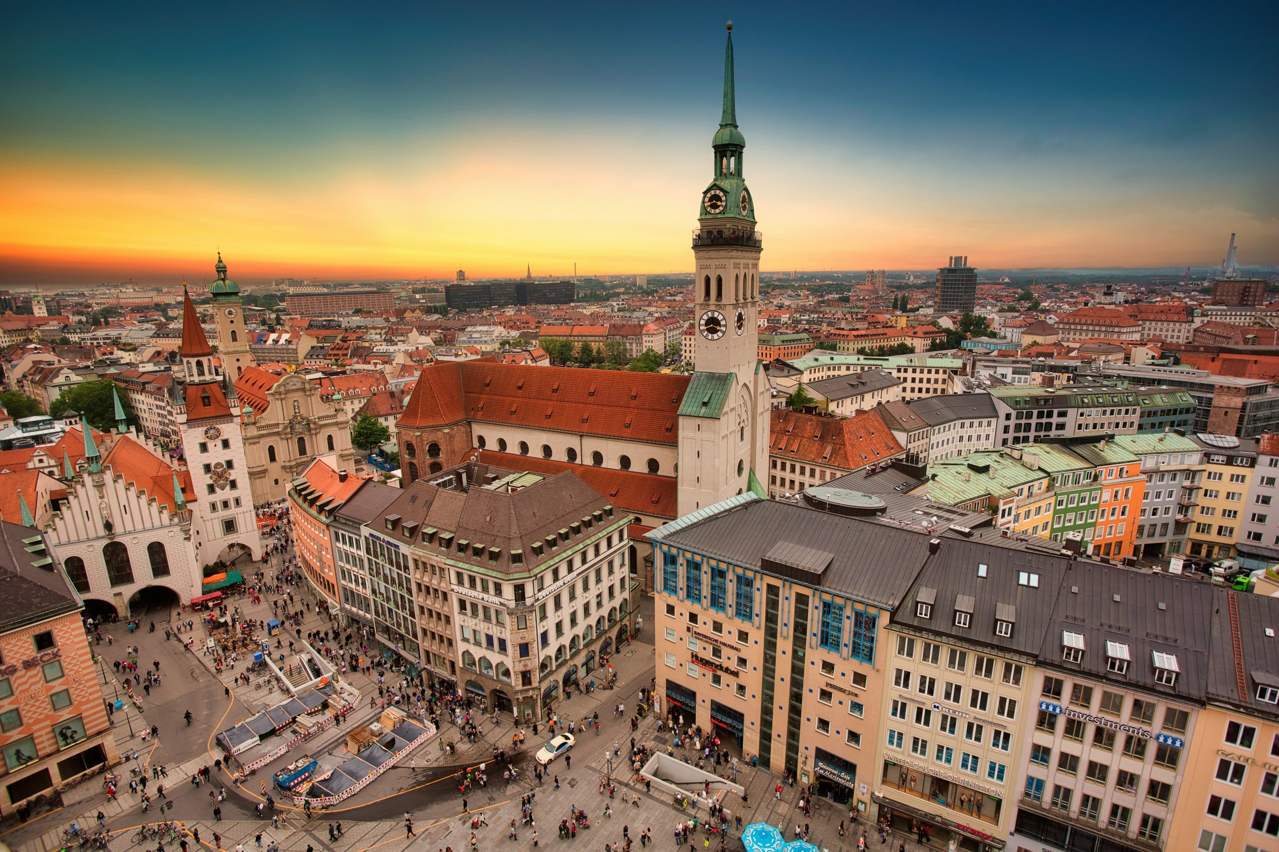 Marienplatz and the surrounding Old Town in Munich viewed from above at sunset with church towers, historic buildings, and people in the square